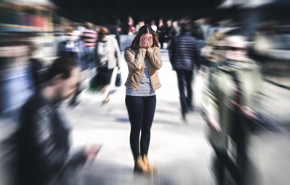 woman in the middle of a blurred crowd covering her face