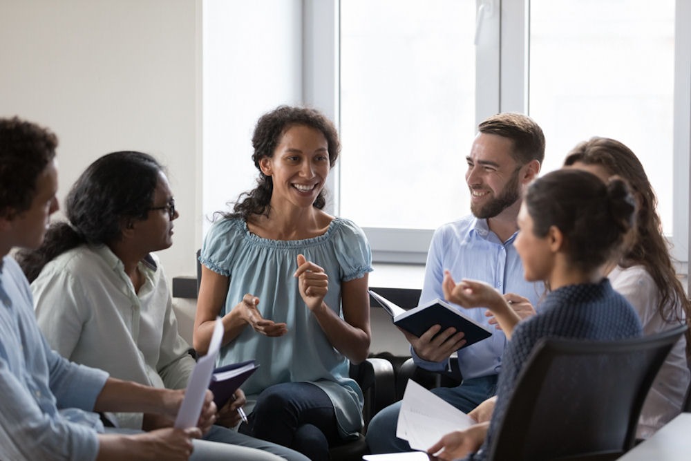 group of adults sitting and smiling while holding notebooks in therapy