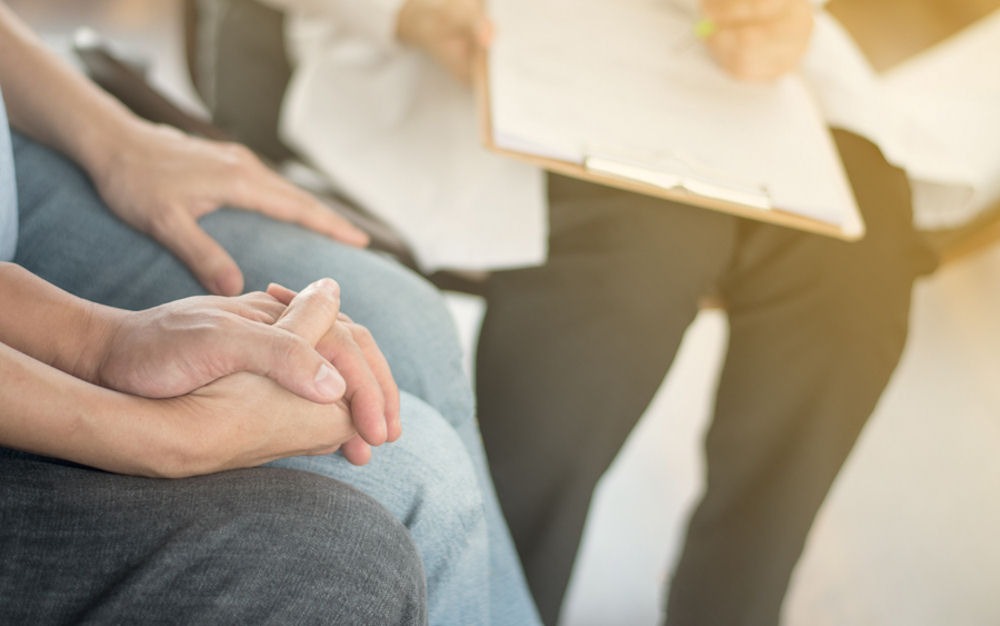 couple holding hands as medical professional fills out form