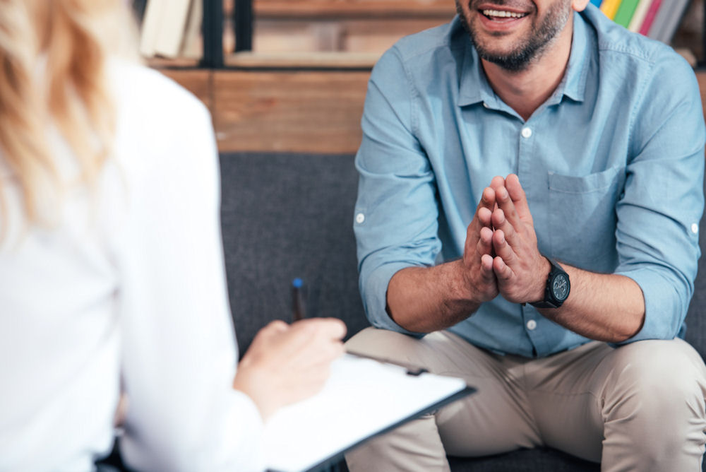 man sitting with hands folded and smiling at counselor as she takes notes