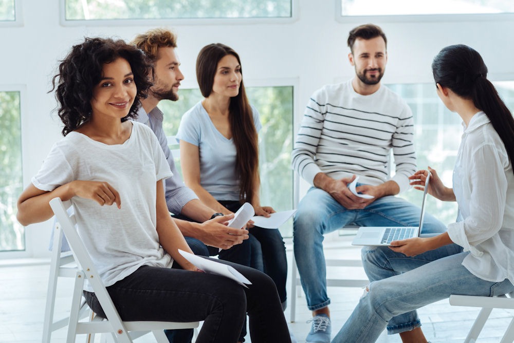 small group of adults sitting in chairs talking while one woman turns toward the camera