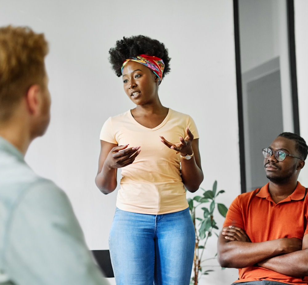 woman standing up and adressing people sitting in a circle