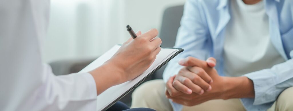 patient folding hands together as doctor writes notes and is sitting across from them