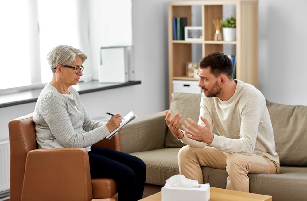 man sitting in therapist's office on a couch talking while she writes notes